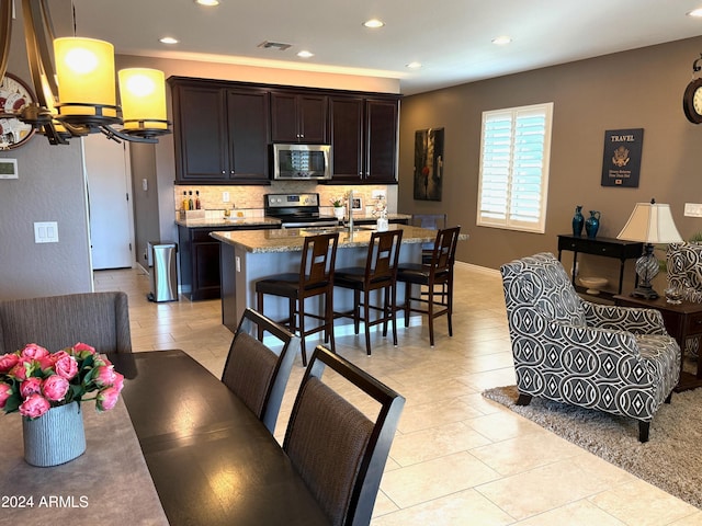 kitchen with a center island with sink, decorative backsplash, light stone countertops, a kitchen bar, and stainless steel appliances