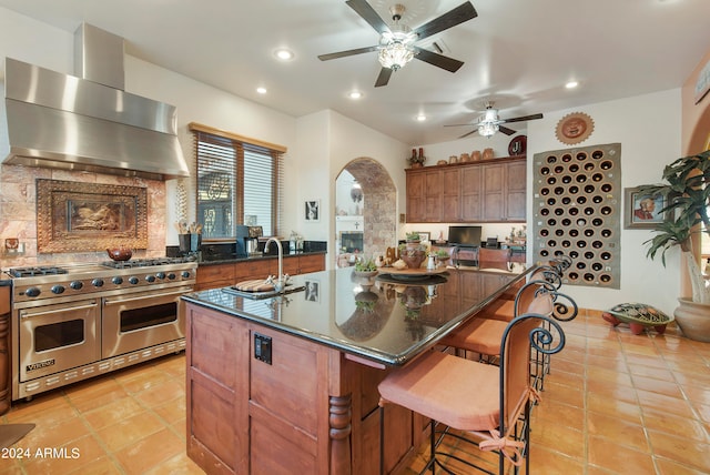 kitchen with a breakfast bar, ceiling fan, double oven range, wall chimney range hood, and a spacious island