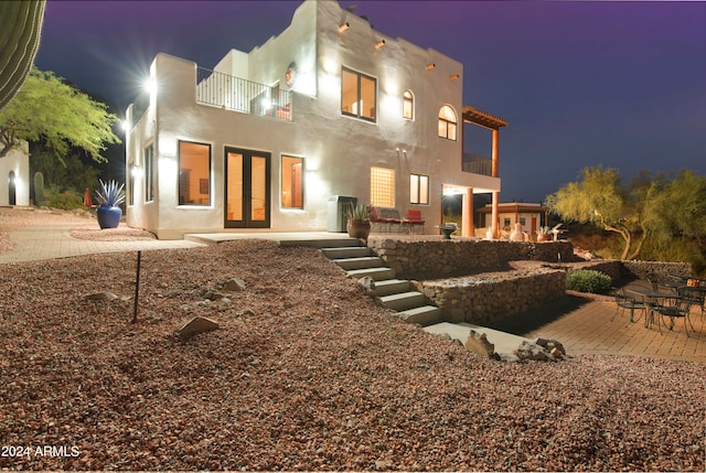 back house at night featuring a balcony and a patio area