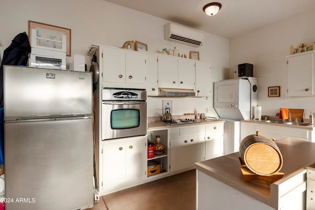 kitchen with sink, an AC wall unit, white cabinetry, stacked washing maching and dryer, and appliances with stainless steel finishes