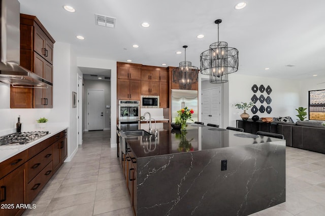 kitchen with an inviting chandelier, wall chimney range hood, a spacious island, and built in appliances