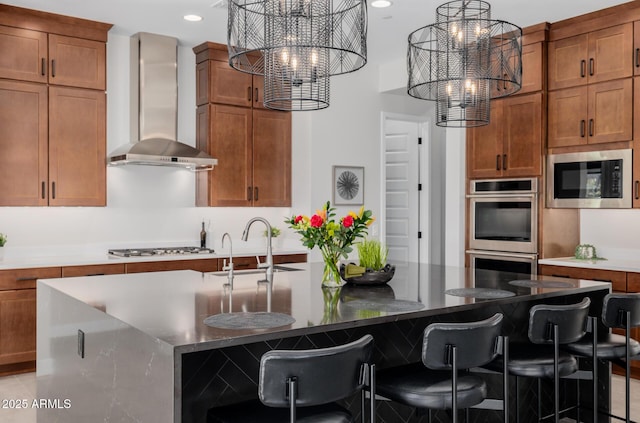 kitchen featuring a center island with sink, built in microwave, wall chimney range hood, a chandelier, and double oven