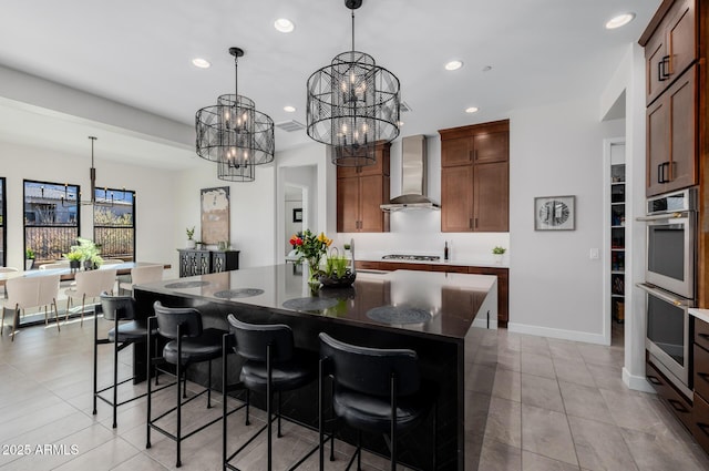 kitchen featuring a kitchen bar, appliances with stainless steel finishes, wall chimney range hood, a kitchen island, and pendant lighting