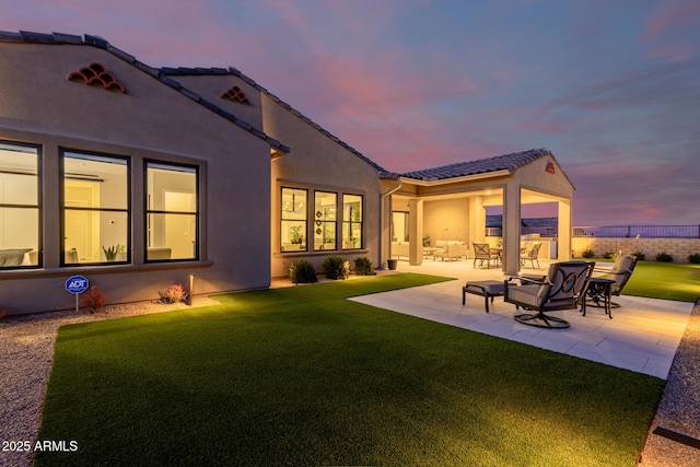 back house at dusk with a patio area and a yard