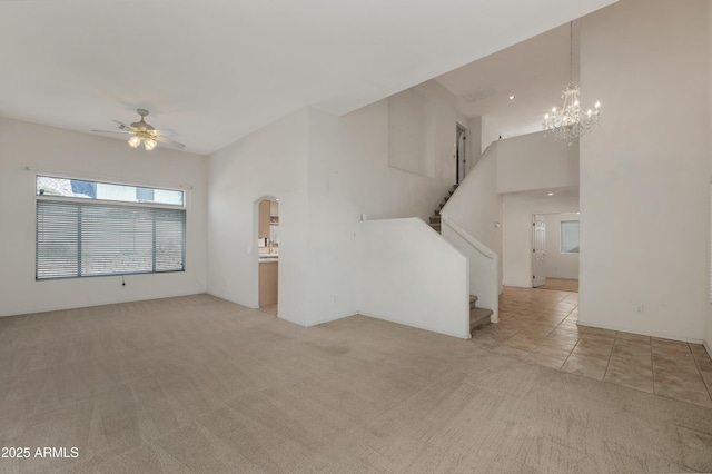 unfurnished living room with ceiling fan with notable chandelier, a towering ceiling, and light colored carpet