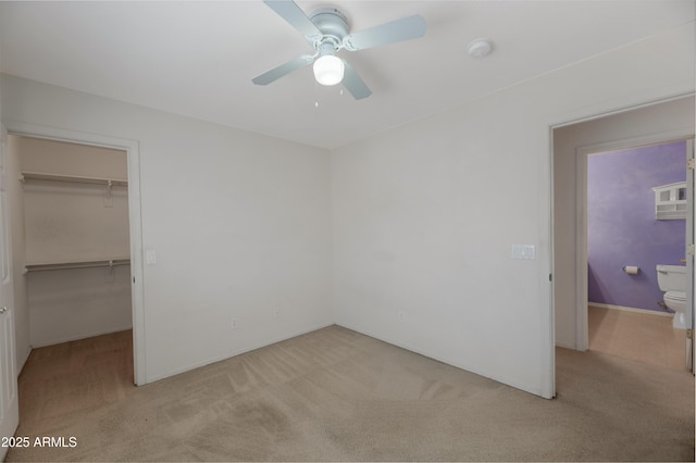 unfurnished bedroom featuring a walk in closet, light colored carpet, a closet, and ceiling fan