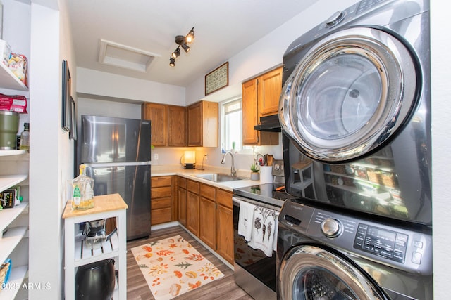 kitchen with sink, stainless steel appliances, dark hardwood / wood-style floors, stacked washer / drying machine, and track lighting