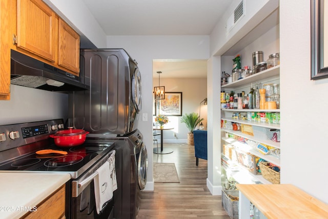 kitchen featuring stainless steel range with electric stovetop, stacked washer and clothes dryer, hanging light fixtures, and light wood-type flooring