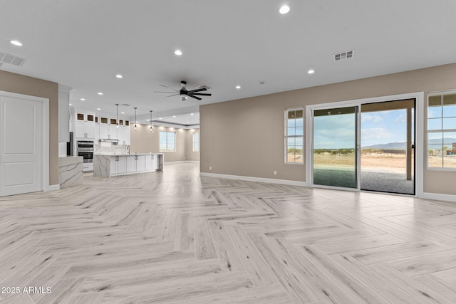 unfurnished living room featuring ceiling fan, light parquet flooring, and plenty of natural light