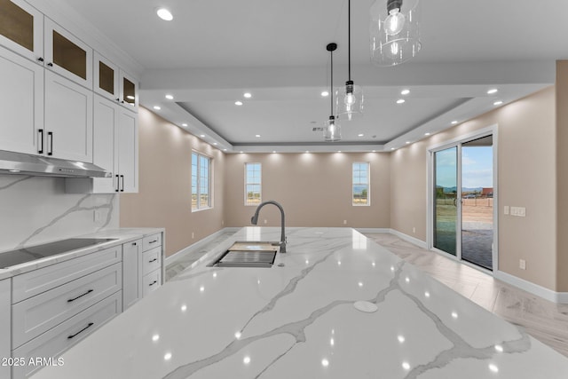 kitchen featuring light stone countertops, white cabinetry, hanging light fixtures, and sink