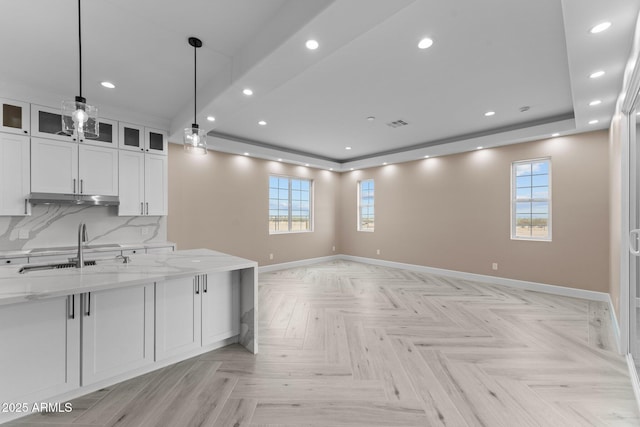 kitchen with decorative light fixtures, white cabinetry, a healthy amount of sunlight, light stone counters, and light parquet floors