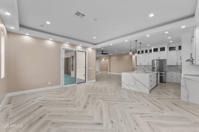 kitchen featuring an island with sink, white cabinets, light stone counters, and stainless steel fridge