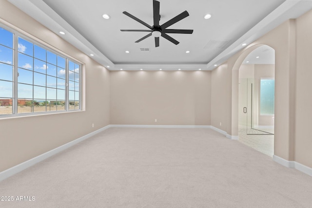 unfurnished room featuring ceiling fan, light colored carpet, and a tray ceiling