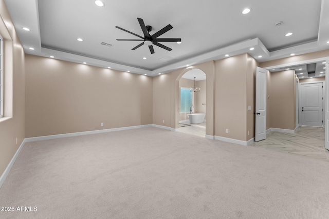 carpeted empty room featuring ceiling fan with notable chandelier and a tray ceiling