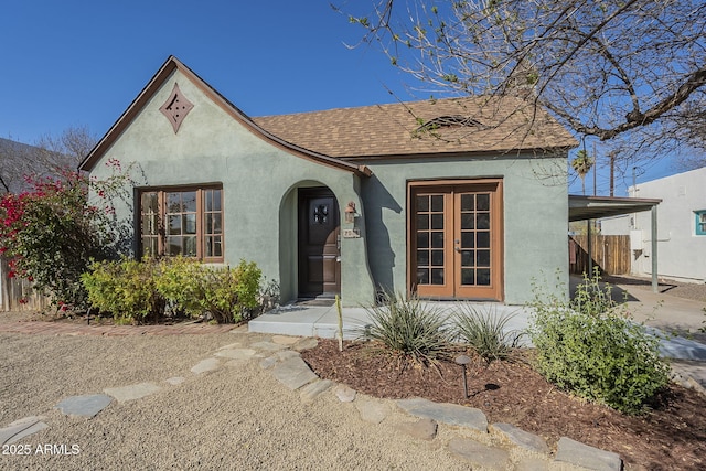 view of front of property featuring french doors, stucco siding, a shingled roof, fence, and an attached carport