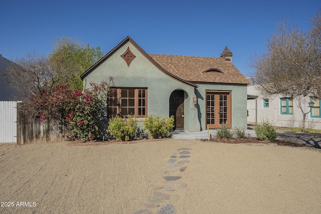 view of front of house with french doors, a shingled roof, fence, and stucco siding