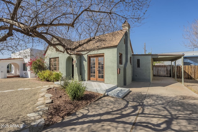 view of front of home with stucco siding, fence, concrete driveway, and french doors