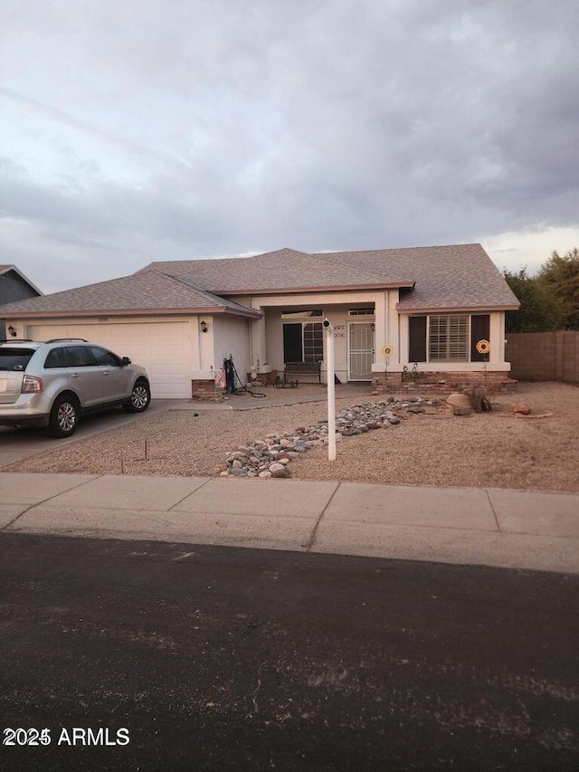 view of front of home with stucco siding, a shingled roof, fence, a garage, and driveway