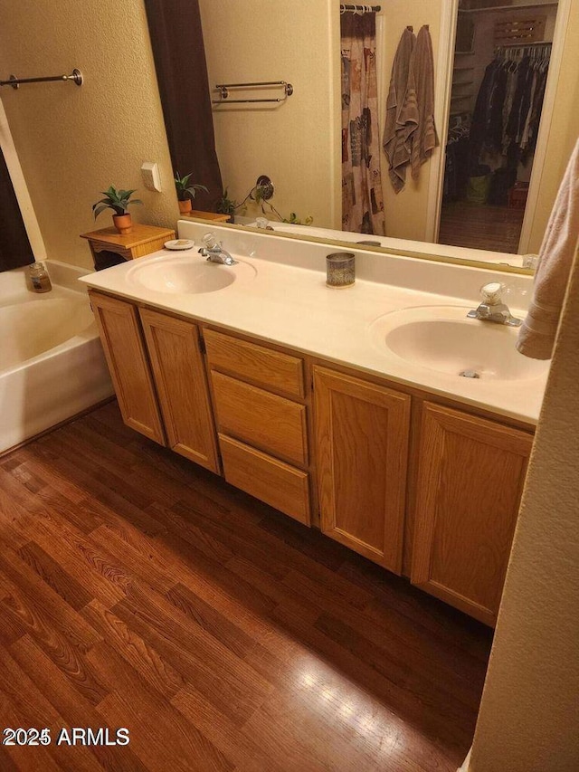 full bath featuring double vanity, a sink, and wood finished floors