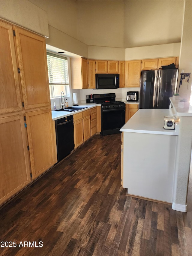 kitchen with a sink, light countertops, light brown cabinetry, black appliances, and dark wood finished floors