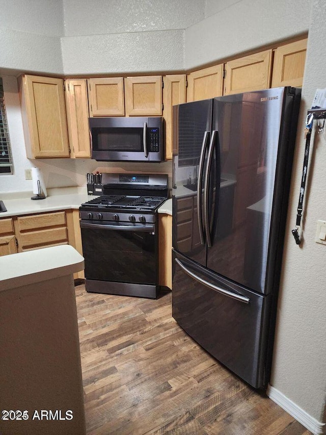 kitchen featuring black appliances, light countertops, wood finished floors, and light brown cabinetry