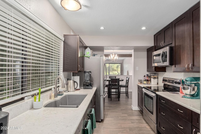 kitchen featuring sink, hanging light fixtures, stainless steel appliances, a notable chandelier, and wood-type flooring