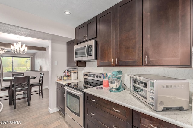 kitchen featuring dark brown cabinetry, light stone countertops, a notable chandelier, appliances with stainless steel finishes, and light wood-type flooring