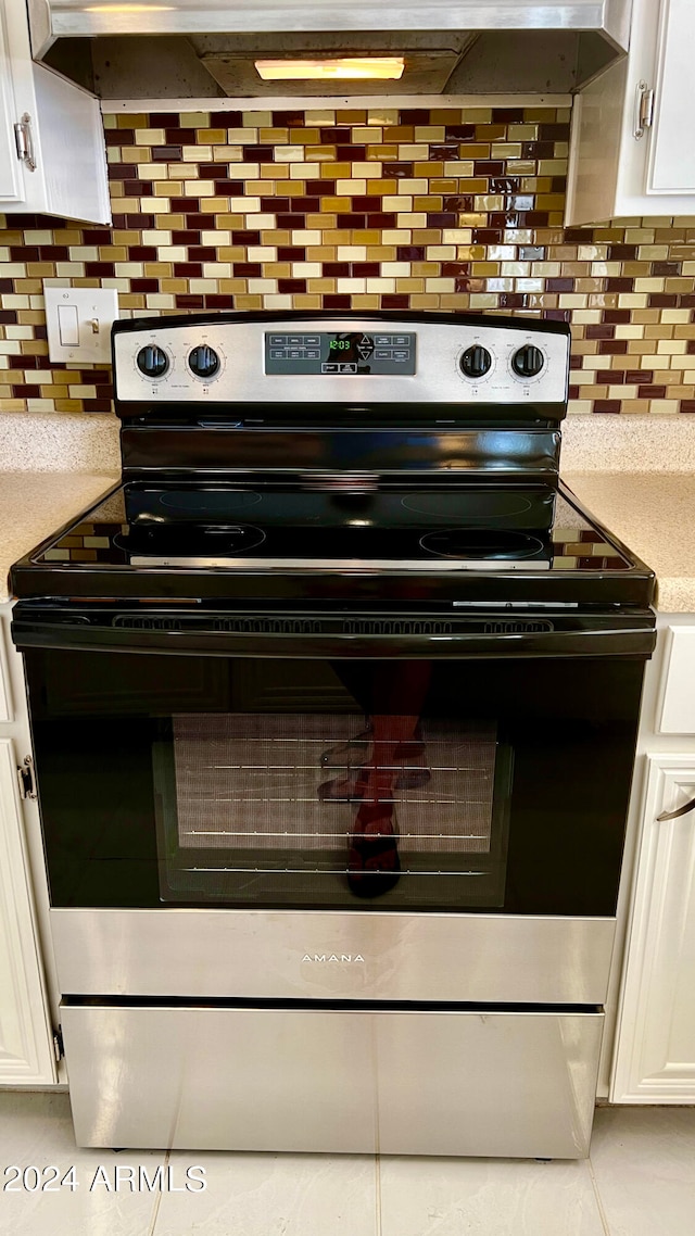 interior details featuring decorative backsplash, white cabinets, and electric stove