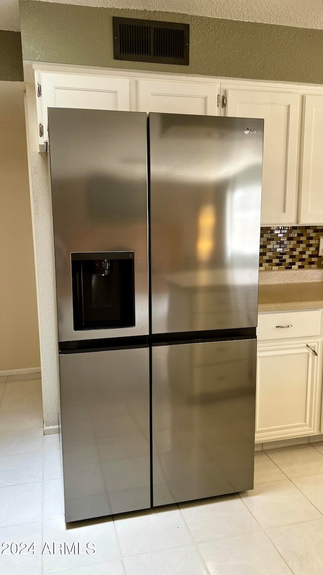 interior details featuring white cabinets, stainless steel refrigerator with ice dispenser, light tile patterned floors, and tasteful backsplash