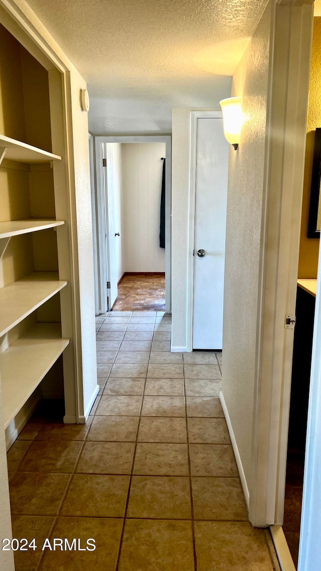 hall with a textured ceiling and tile patterned floors