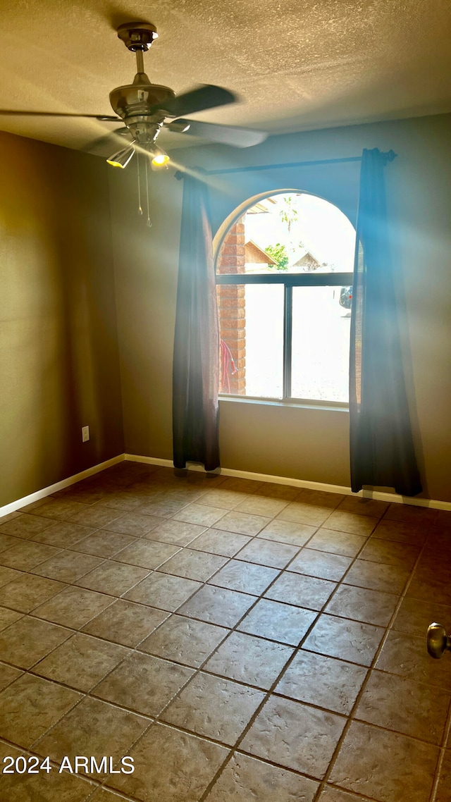 spare room with ceiling fan, a textured ceiling, and tile patterned flooring