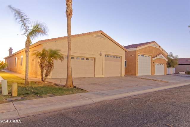 view of front facade with a garage, driveway, a tiled roof, and stucco siding