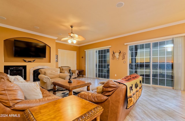 living room featuring ceiling fan, light wood-style floors, a fireplace, and crown molding