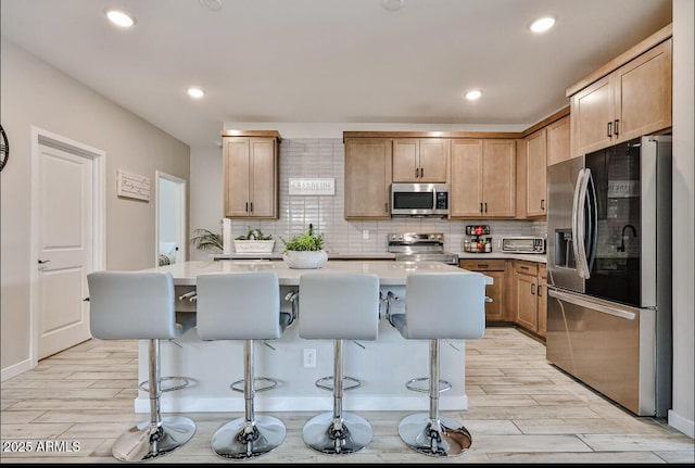 16955 W Butler Ave, Waddell, AZ 85355 - kitchen with stainless steel appliances, light wood finished floors, light countertops, a breakfast bar area, and recessed lighting