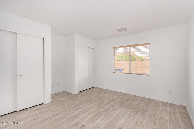 12132 W Dahlia Dr, El Mirage, AZ 85335 - unfurnished bedroom with light wood-type flooring, two closets, and baseboards