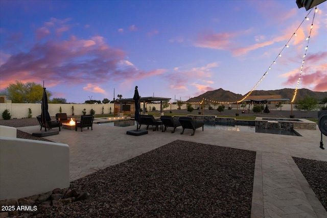 20715 E Watford Dr, Queen Creek, AZ 85142 - patio terrace at dusk featuring an outdoor fire pit, an in-ground hot tub, a mountain view, and a fenced backyard