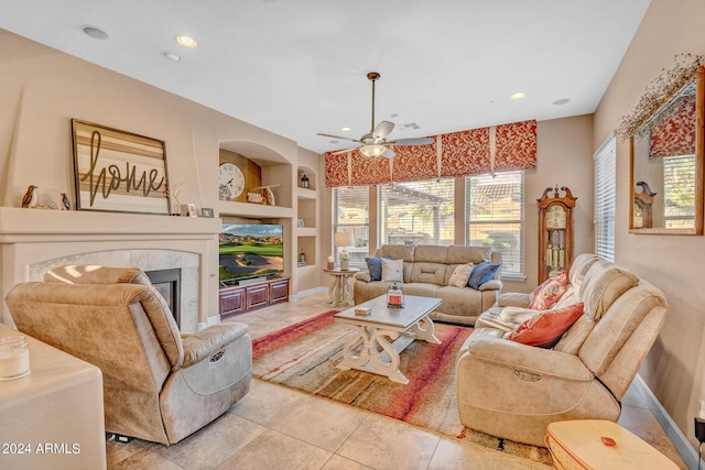 living area featuring a fireplace, a ceiling fan, tile patterned floors, baseboards, and built in shelves