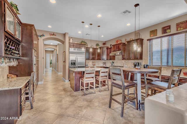 kitchen with visible vents, arched walkways, under cabinet range hood, stainless steel built in refrigerator, and decorative backsplash