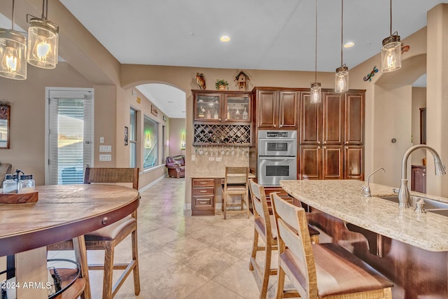 kitchen with tasteful backsplash, light stone countertops, arched walkways, double oven, and a sink