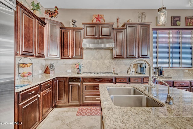 kitchen with tasteful backsplash, under cabinet range hood, light stone counters, a sink, and stainless steel appliances