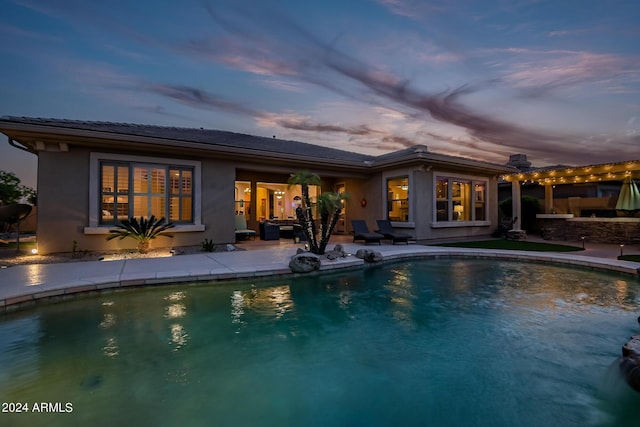 back of house at dusk featuring an outdoor pool, a patio area, and stucco siding