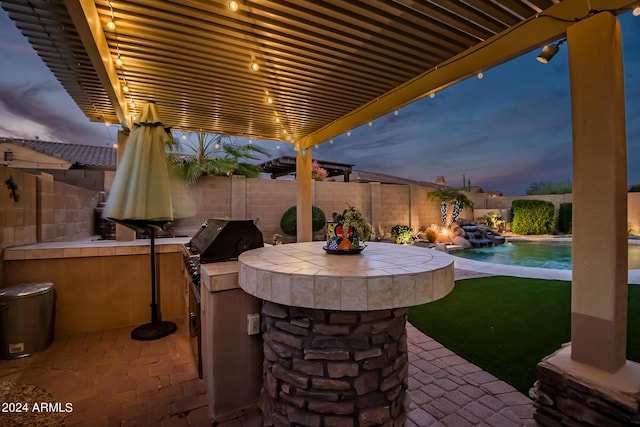 patio terrace at dusk featuring a fenced in pool, outdoor dry bar, an outdoor kitchen, area for grilling, and a fenced backyard
