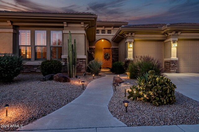 view of front facade with an attached garage, a tiled roof, stucco siding, and stone siding