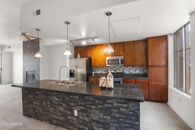 kitchen featuring sink, a center island with sink, dark stone countertops, appliances with stainless steel finishes, and pendant lighting