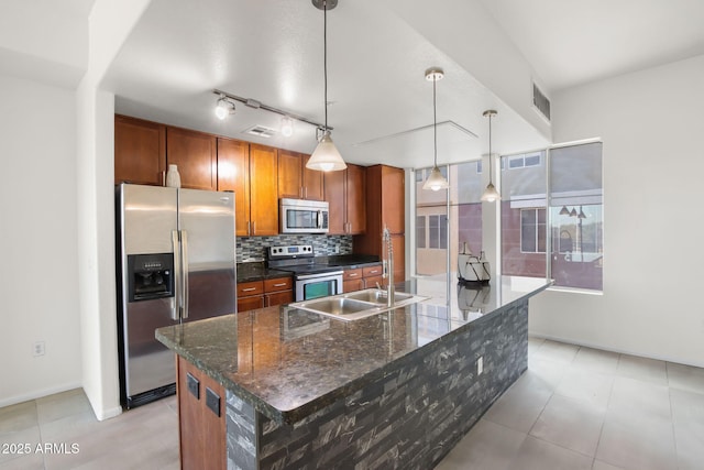 kitchen featuring appliances with stainless steel finishes, decorative light fixtures, sink, decorative backsplash, and a center island with sink