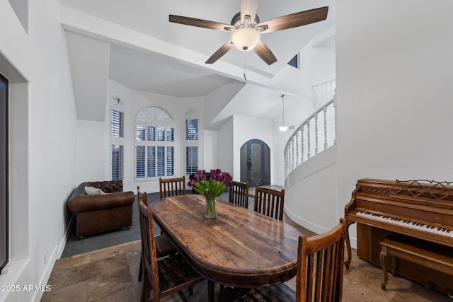 dining room featuring arched walkways, stairs, stone finish flooring, baseboards, and a ceiling fan