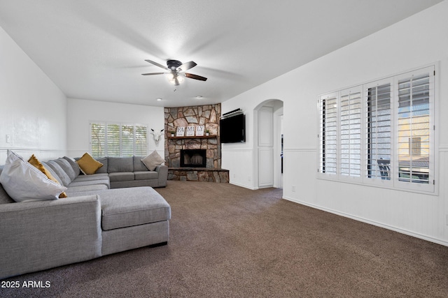 carpeted living area with arched walkways, ceiling fan, wainscoting, and a fireplace