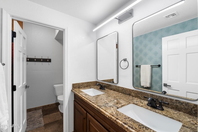 bathroom with double vanity, visible vents, toilet, and a sink