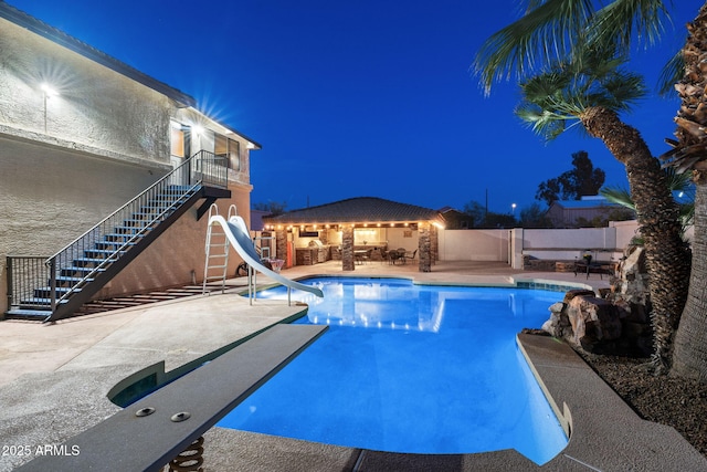 pool at twilight with a patio, stairs, a water slide, and fence
