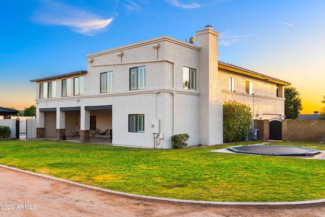 back of property at dusk featuring a patio, fence, stucco siding, and a chimney
